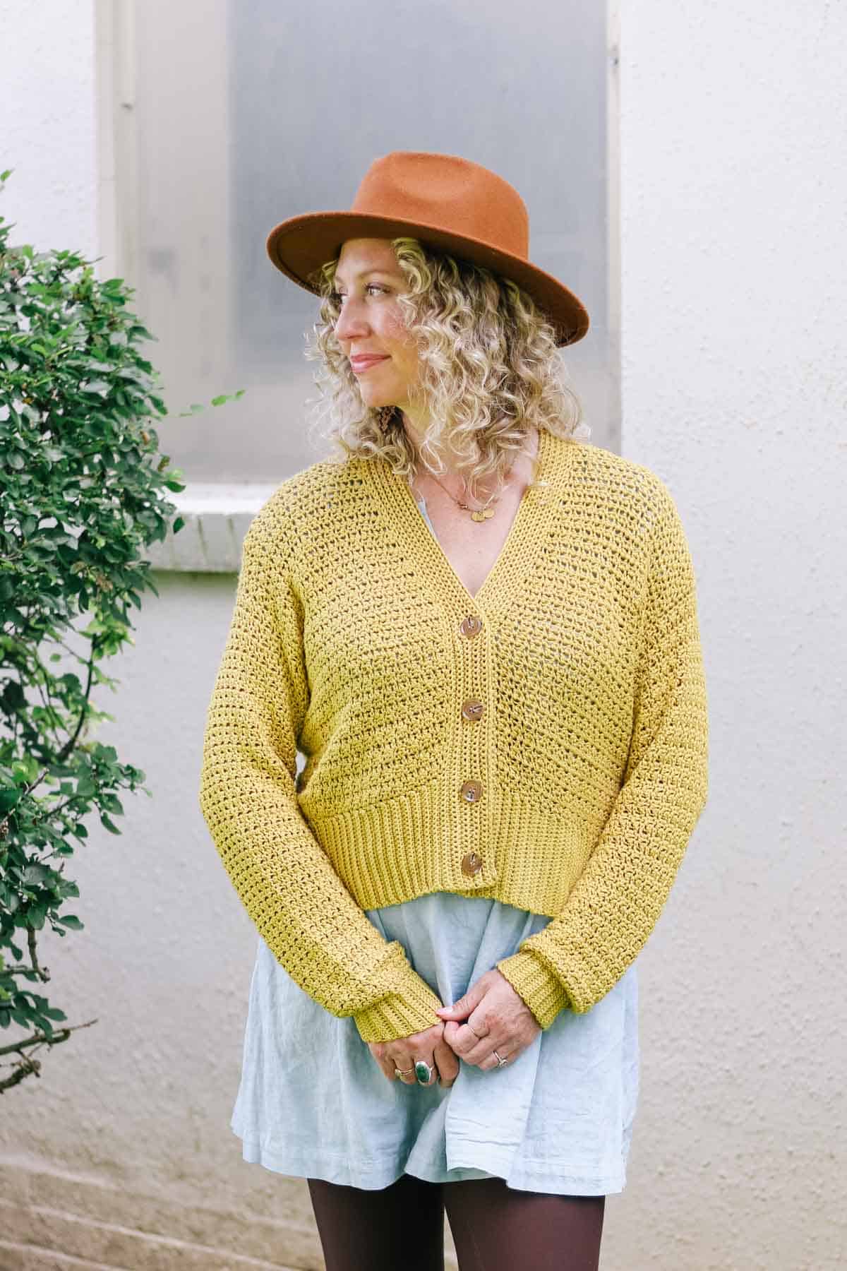 Woman wearing a yellow shorter crocheted cardigan.