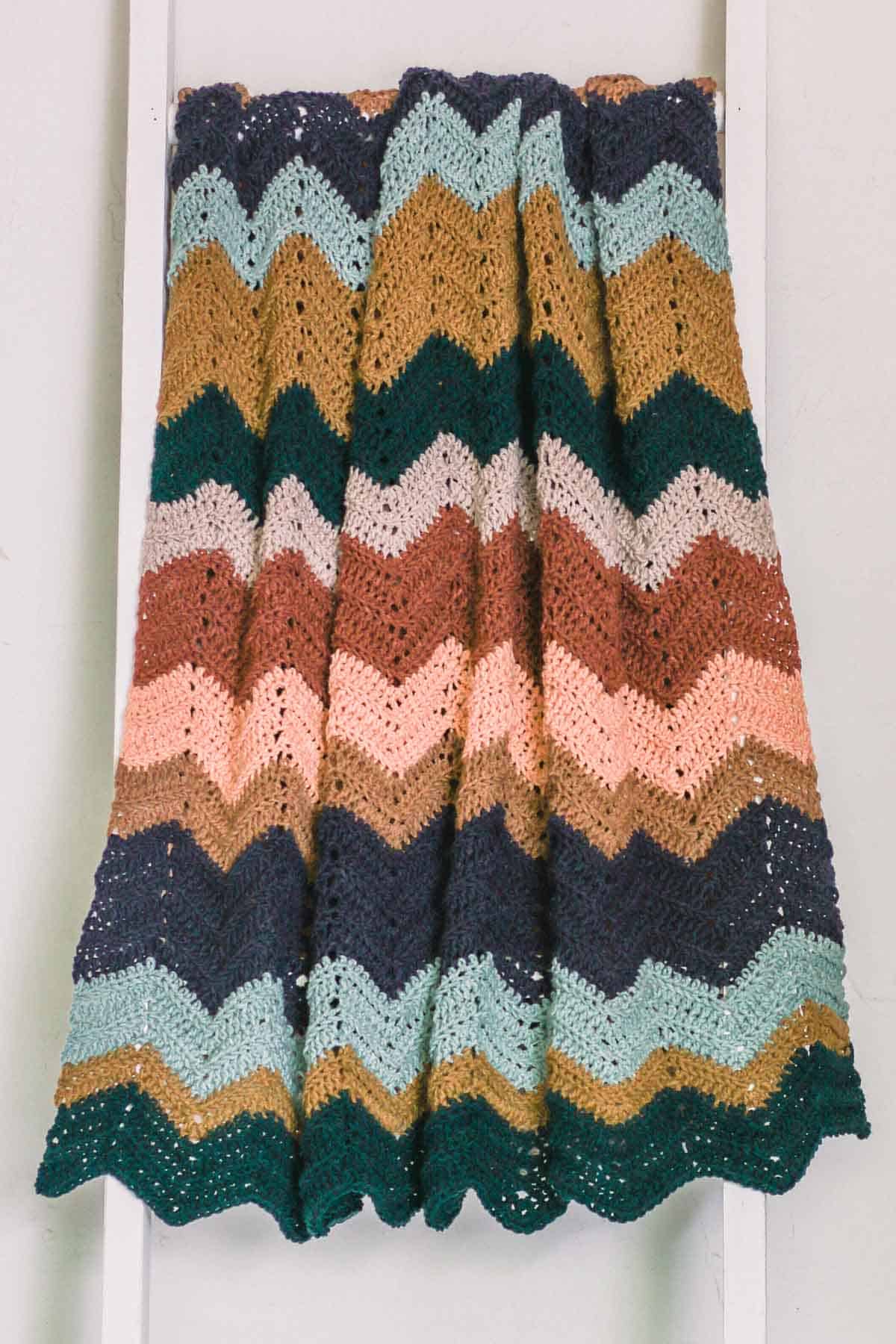 A multi-color crochet zig zag blanket draped over a ladder.