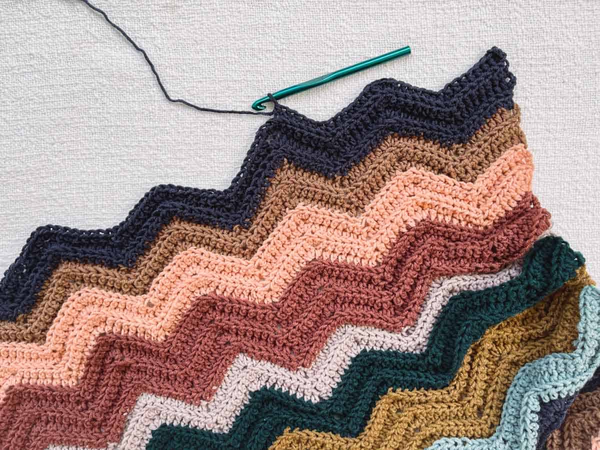 An in-progress striped crochet chevron blanket in muted colors.