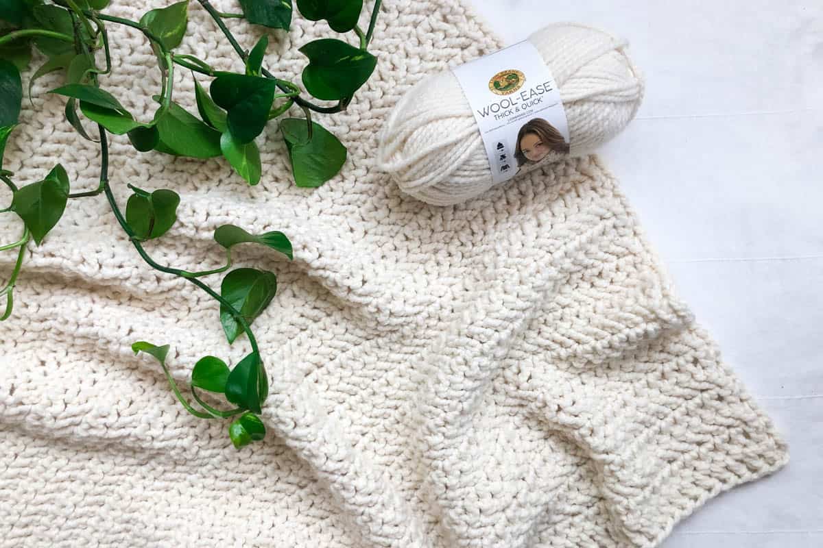 A cream-colored chunky crochet throw blanket made with easy stitches.