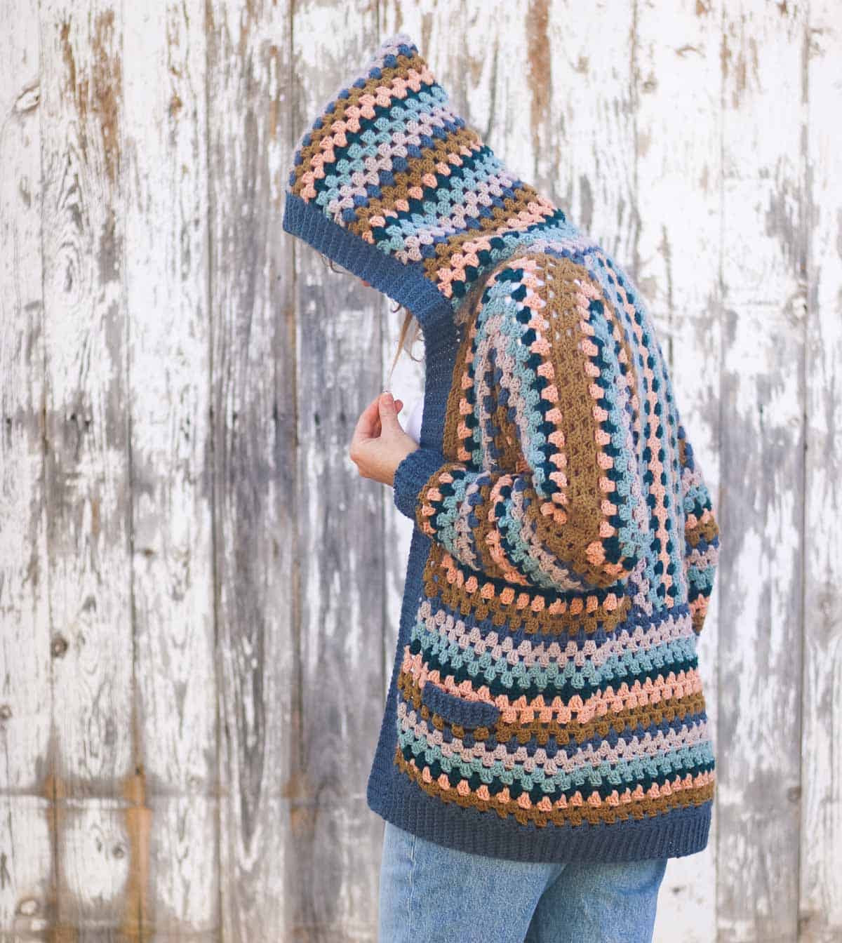 Woman wearing a crocheted hexagon cardigan with a hood hiding her face.