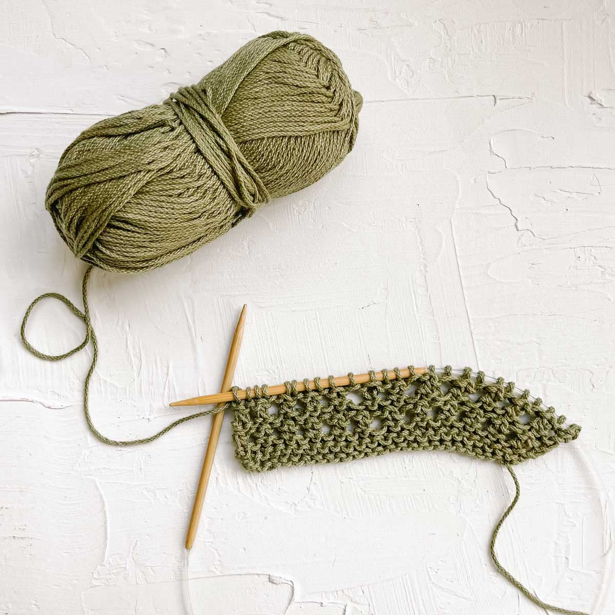 Circular knitting needles with flat square of green yarn and knitting.