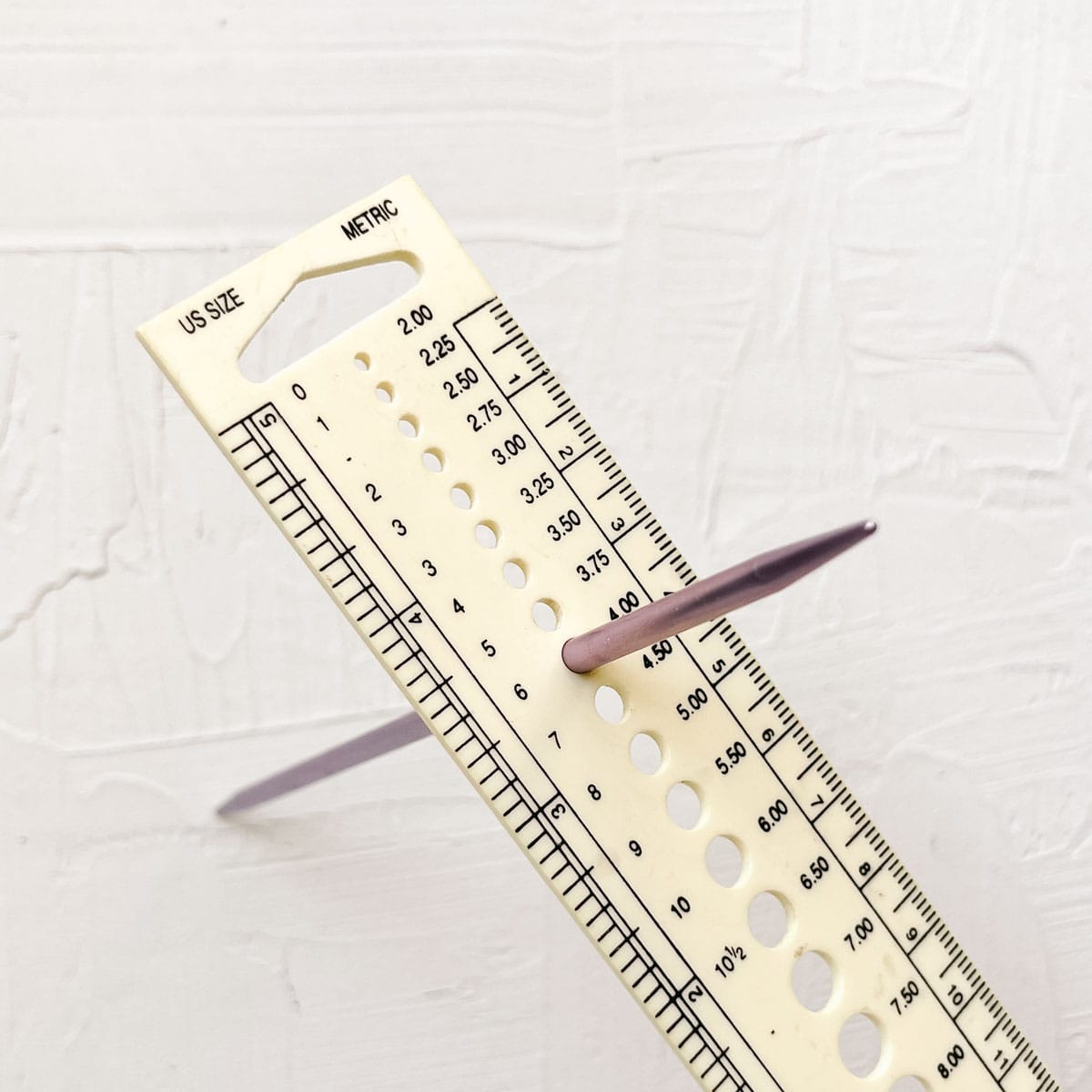 A knitting needle gauge measuring the diameter of a DPN.