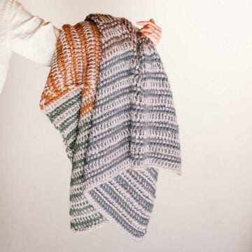An outstretched arm holding a striped Tunisian crochet blanket.