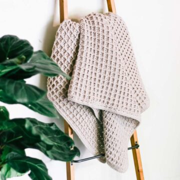 A crocheted waffle stitch blanket hanging on a wooden ladder.