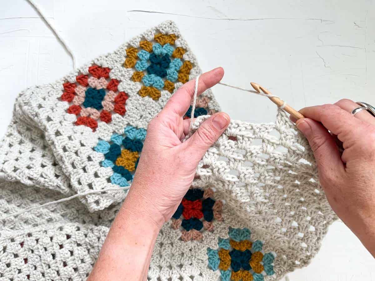 Close-up of hands crocheting rows of granny stitches.