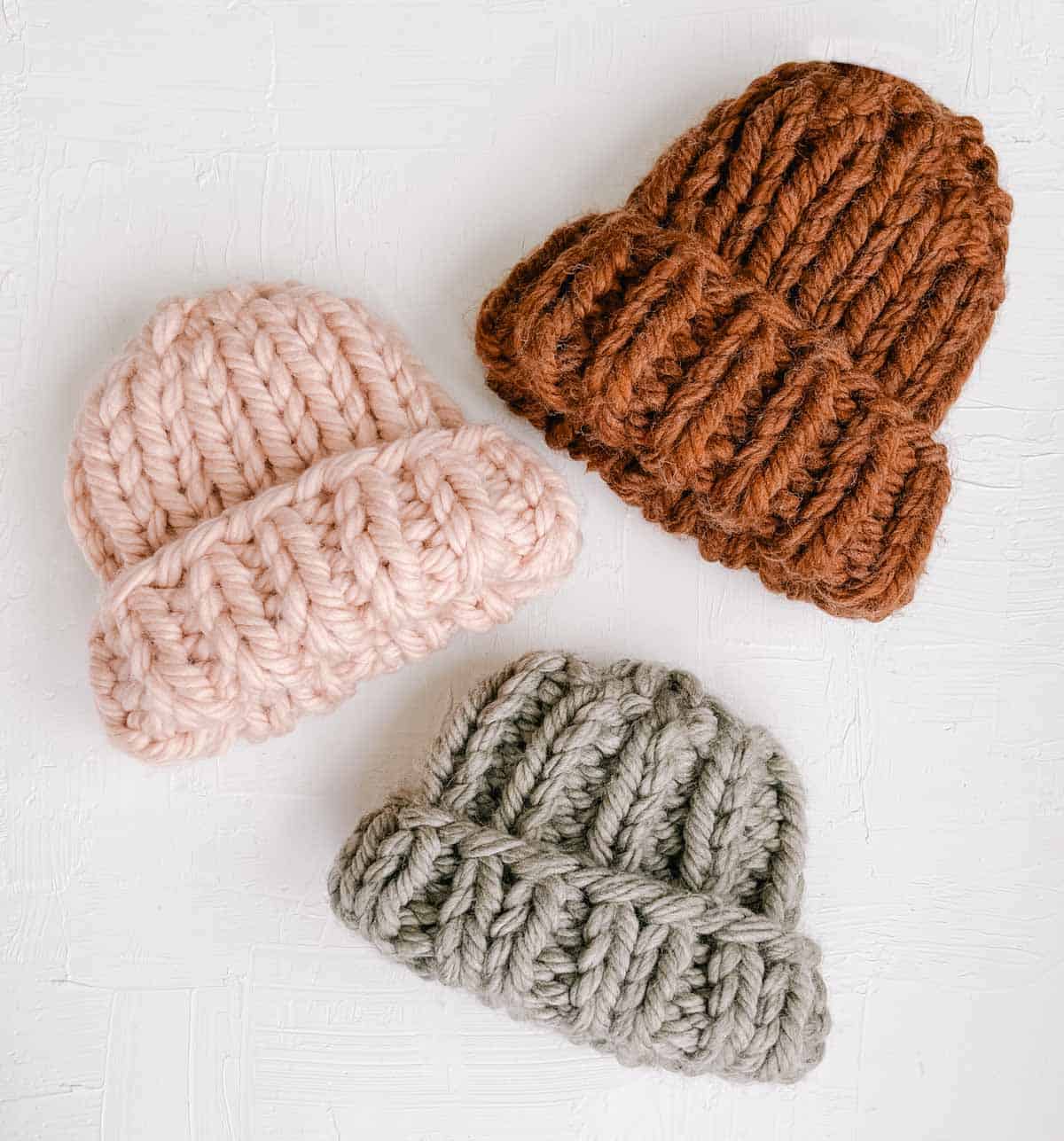 Three bulky knit beanies next to each other on a white background.