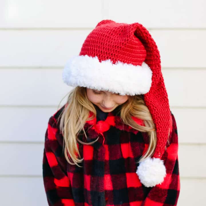 A young girl wearing a crochet Santa beanie and a Christmas jacket.
