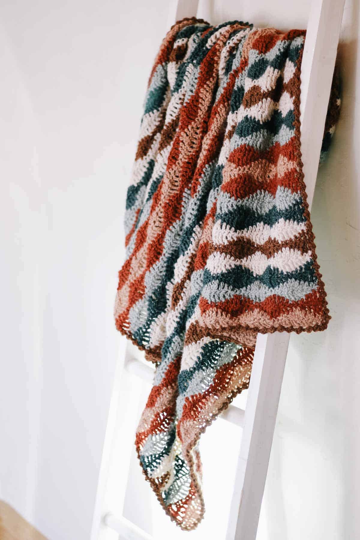 A wavy crochet blanket hanging on a white ladder.