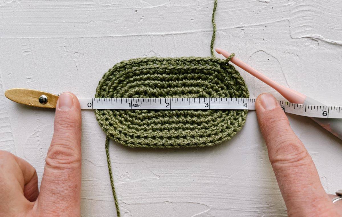 Crochet baby bootie sole being measured to assure accurate gauge.
