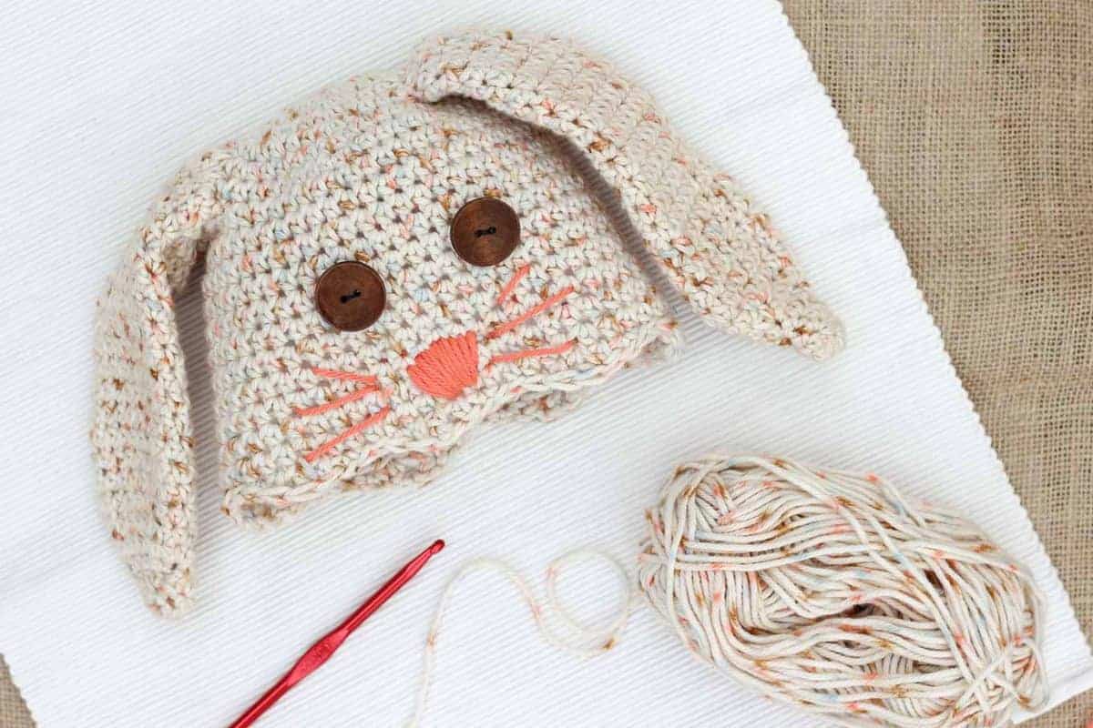 Crochet bunny hat with a skein of yarn and crochet hook.