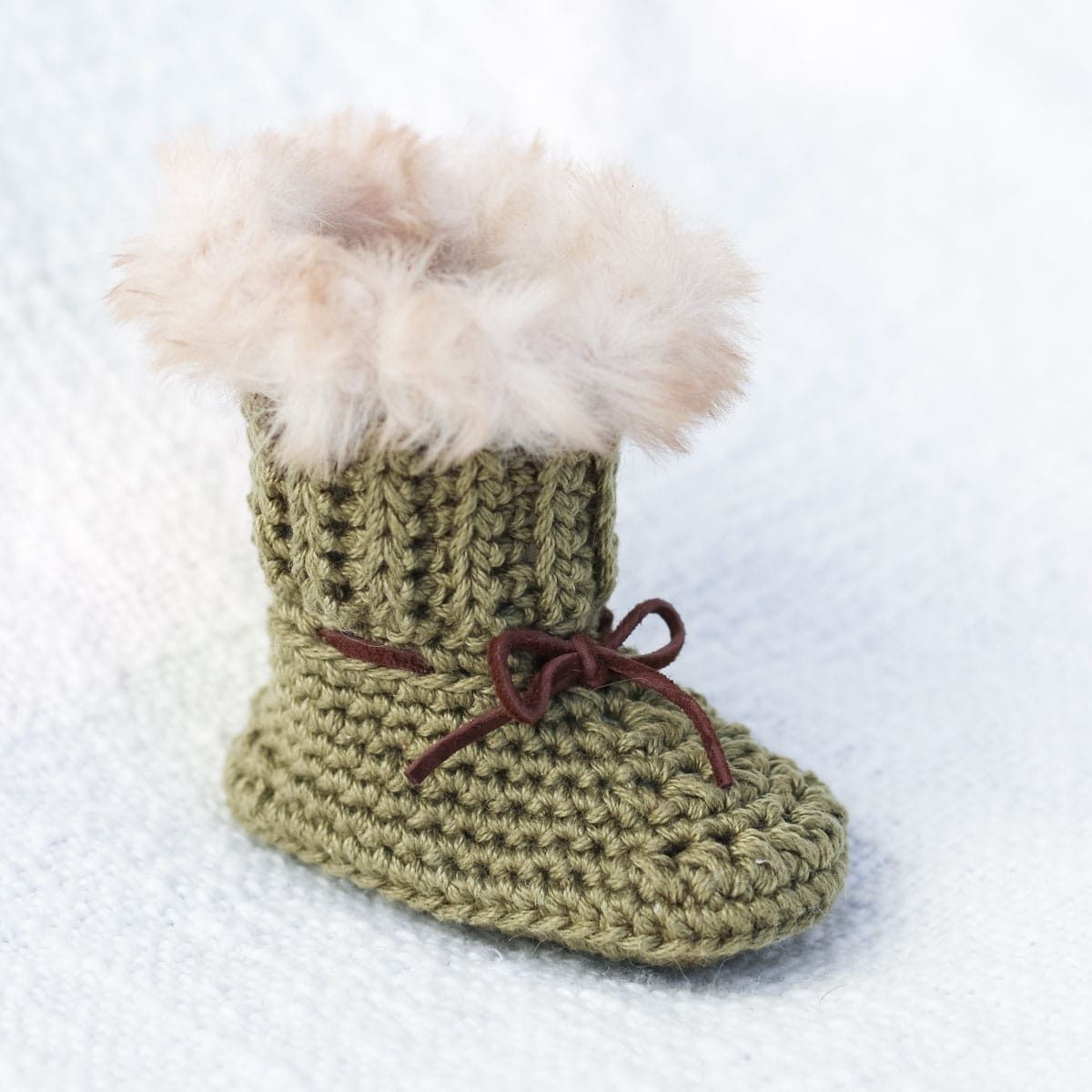 Green crochet baby bootie with fur trim and leather.