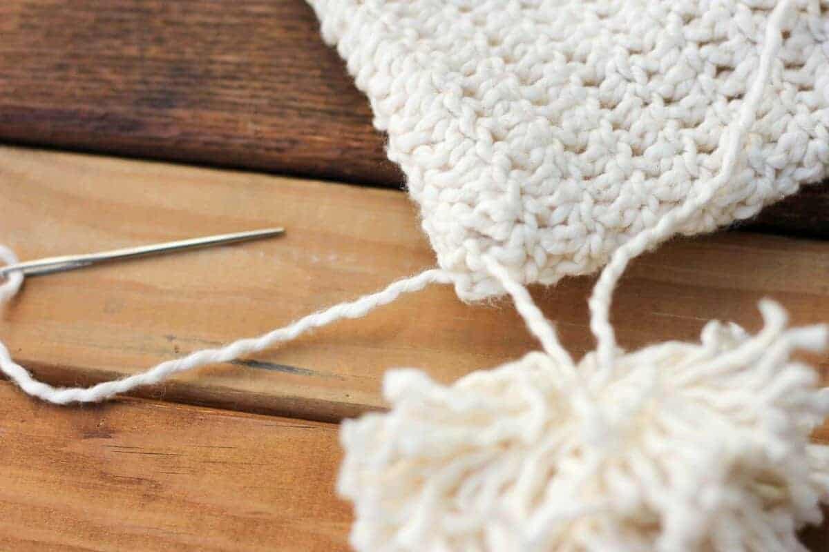 A yarn pom pom being attached to a crochet hat.