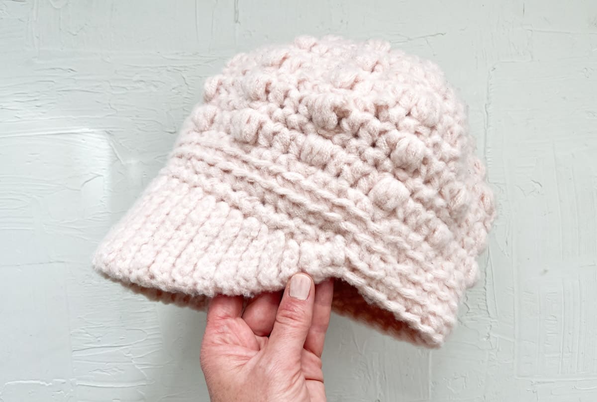 Crocheted newsboy hat with puff stitches held by a caucasian hand.