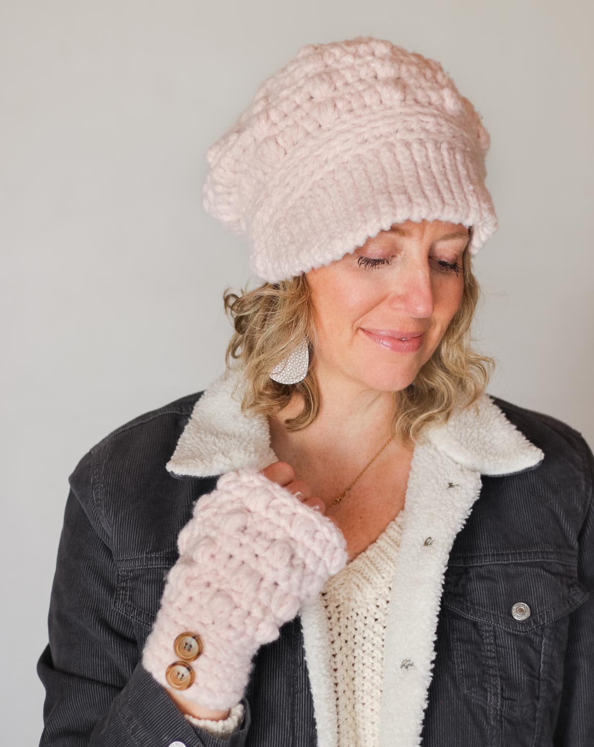Matching set of crocheted newsboy hat and hand warmers modeled by a woman indoors.