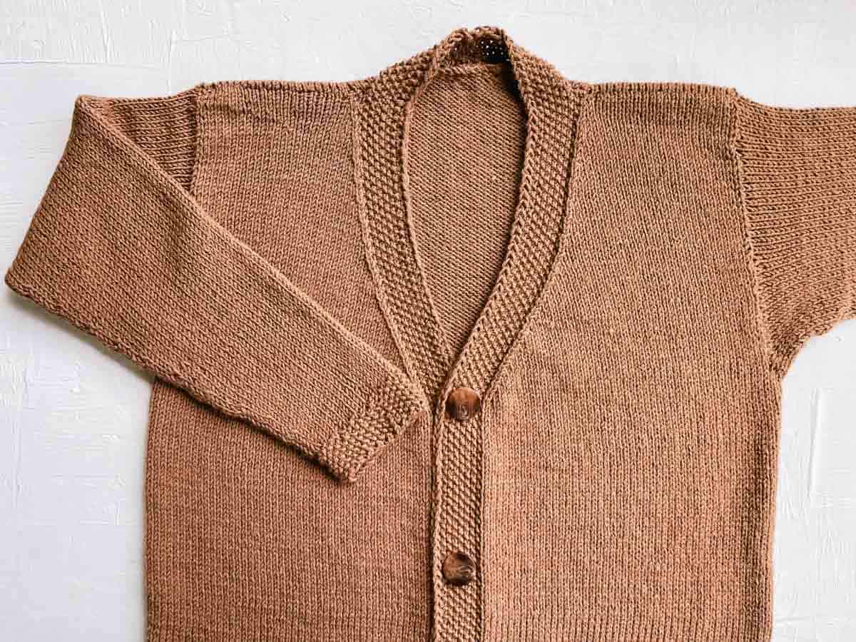 Stockinette cardigan with buttons and tapered collar, laying flat.