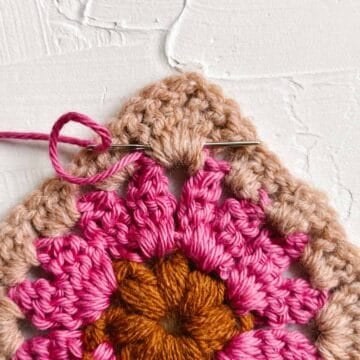 Tapestry needle weaving yarn tail through crocheted granny square stitches.