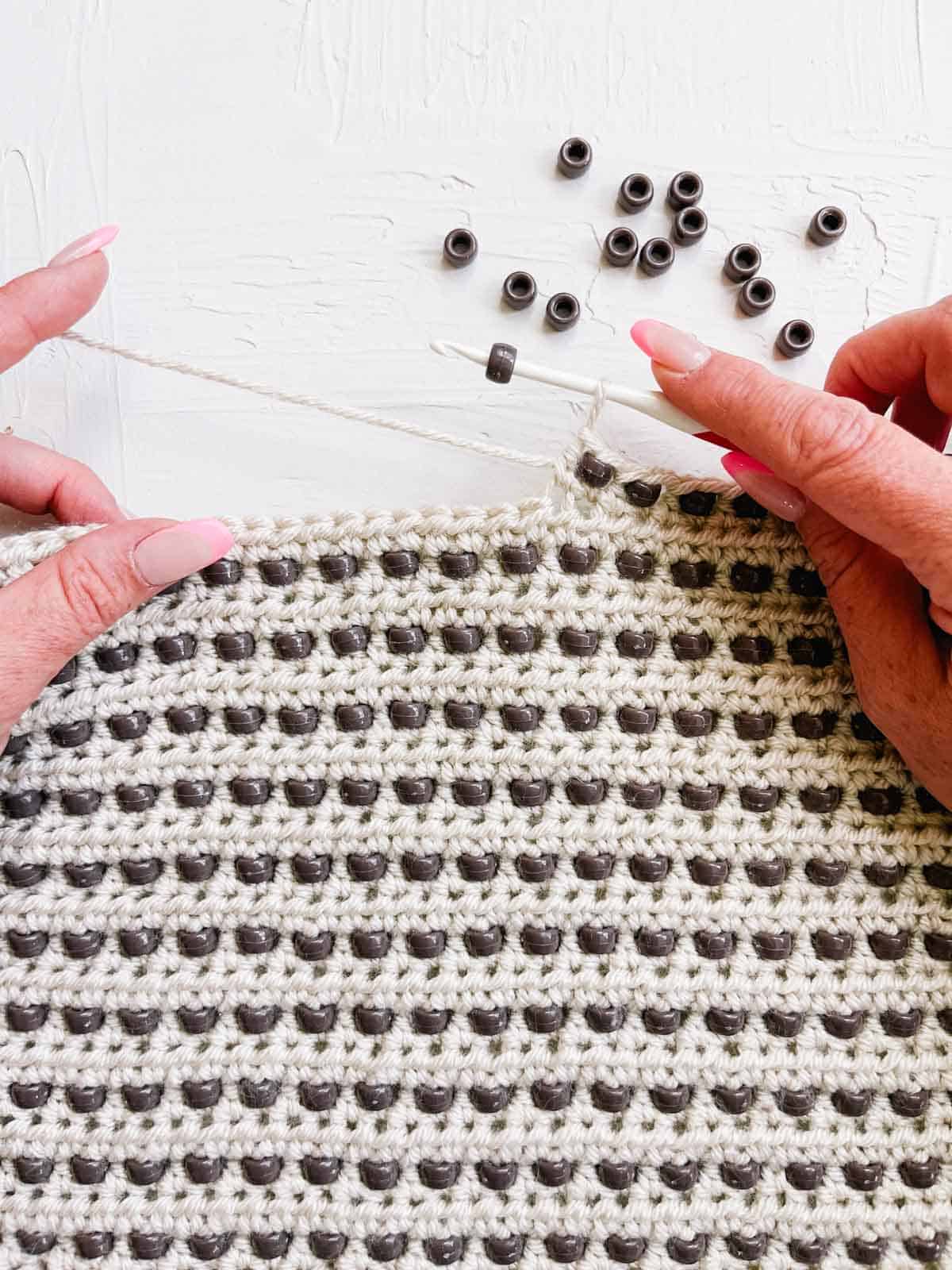 A crocheted blanket with brown pony beads being added to the stitches.