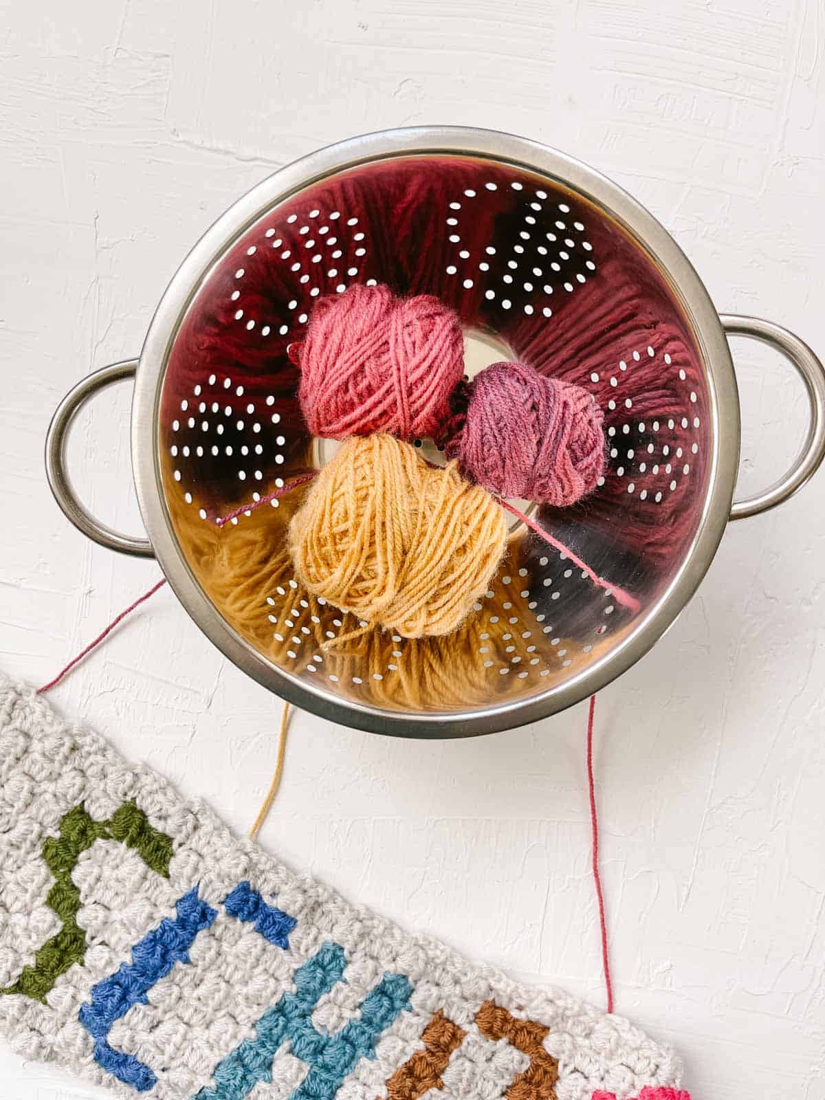 Multiple balls of yarn threaded through the holes of a kitchen colander. 