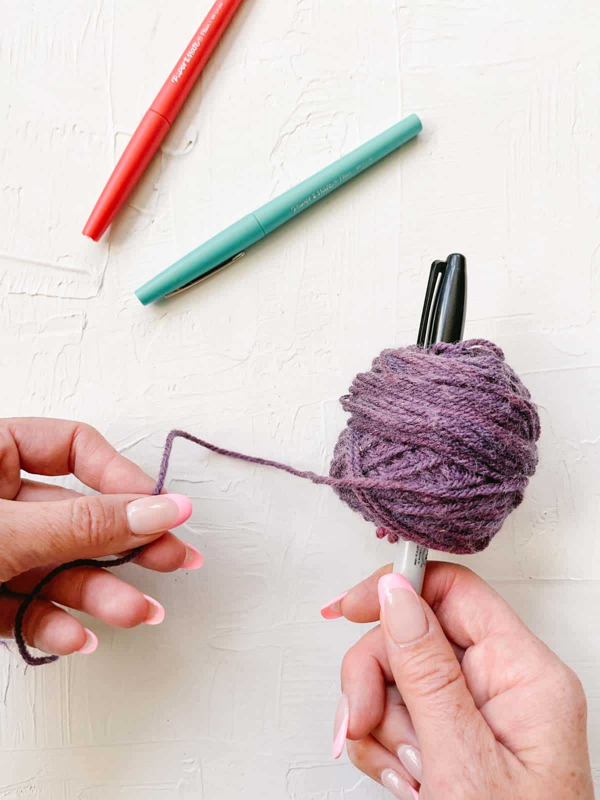 Winding scraps of yarn on a sharpie pen to create a yarn ball.