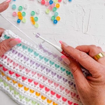 Woman's hands adding colorful pony beads to a row of crocheting.