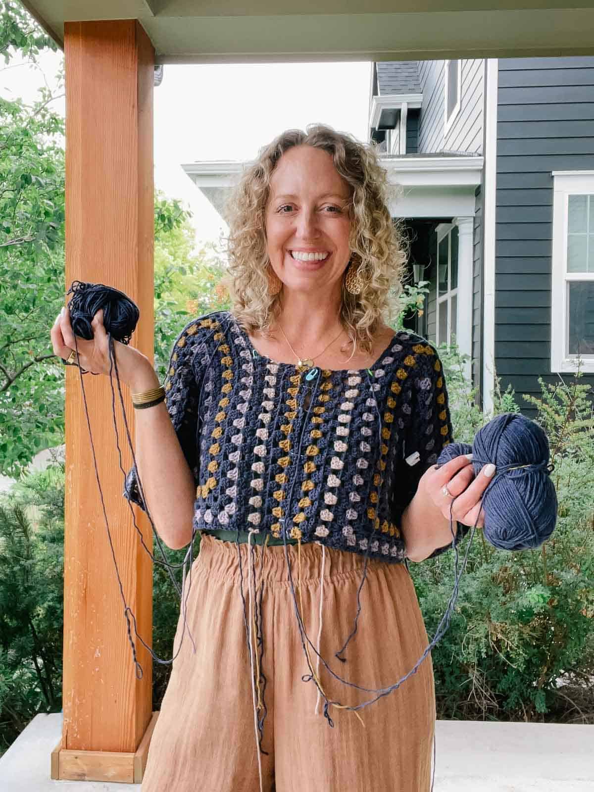 An in-progress crochet hexagon dress worn by a blonde woman while holding yarn skeins.