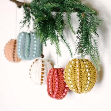 Crocheted ornaments with plastic beads hanging from a branch.