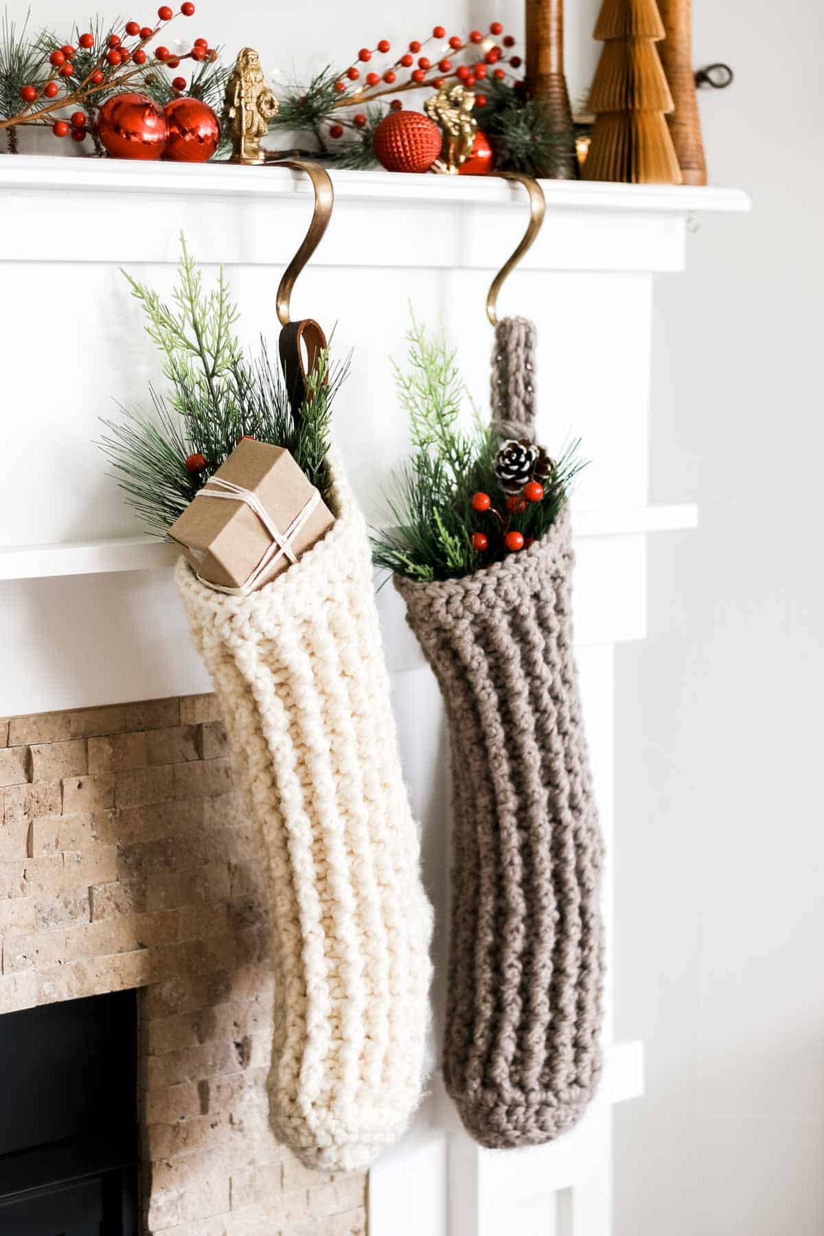 Two Christmas crochet stockings filled with decor hung by the fireplace.