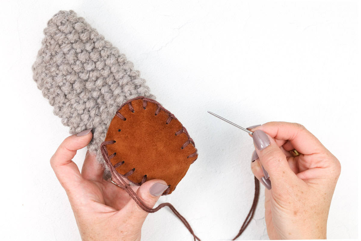 Rectangle slippers with a woman sewing a leather sole into it.
