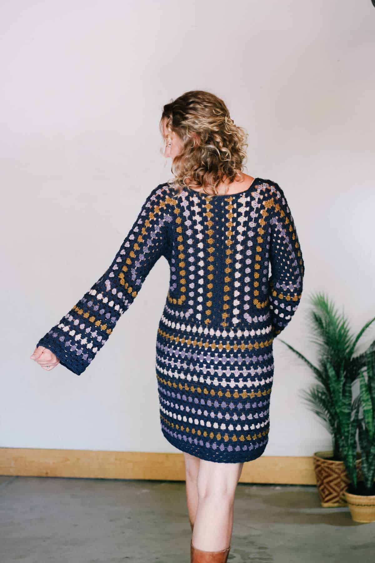 A crochet granny stitch dress worn by a blonde woman and a pair of brown leather boots with her back to the camera.