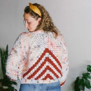 An easy c2c cardigan for beginners with an arrow motif worn by a blonde woman with her back to the camera.