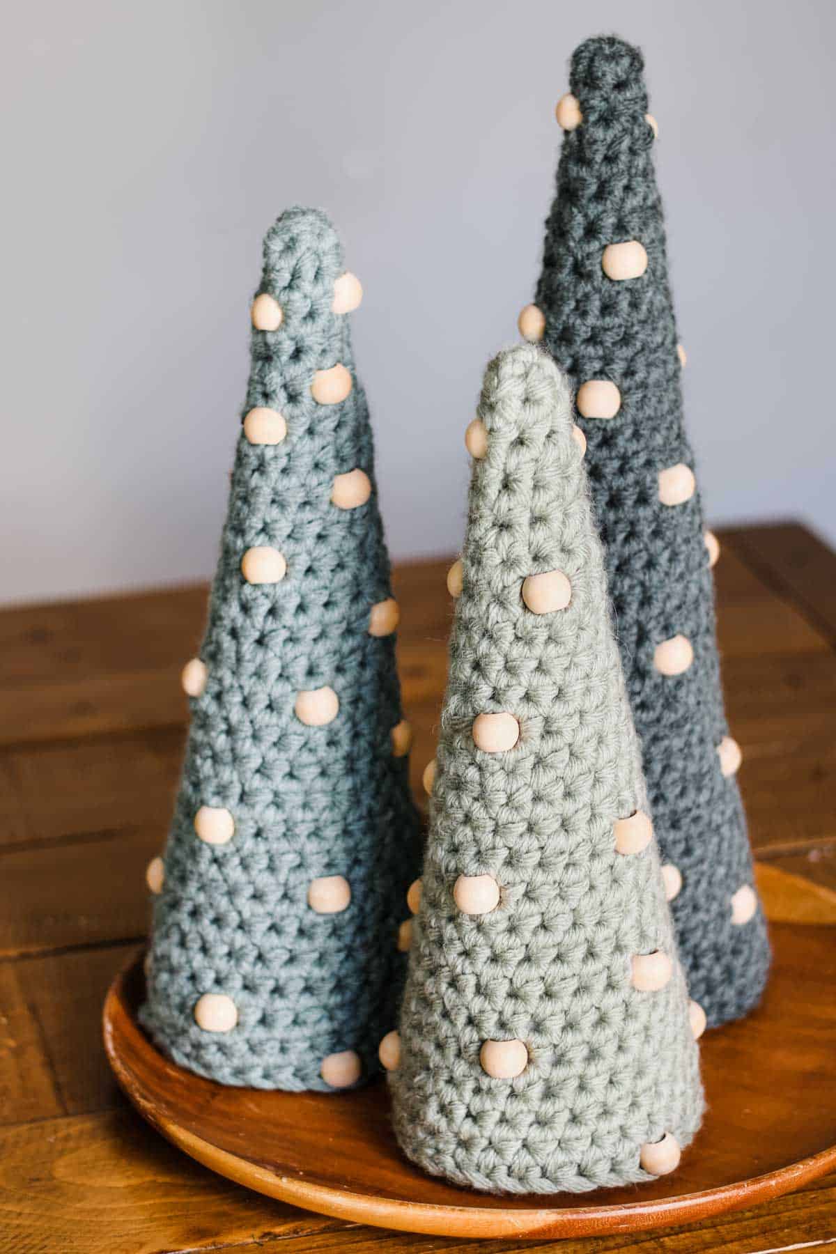 Three crochet Christmas trees with beads on a wooden plate.