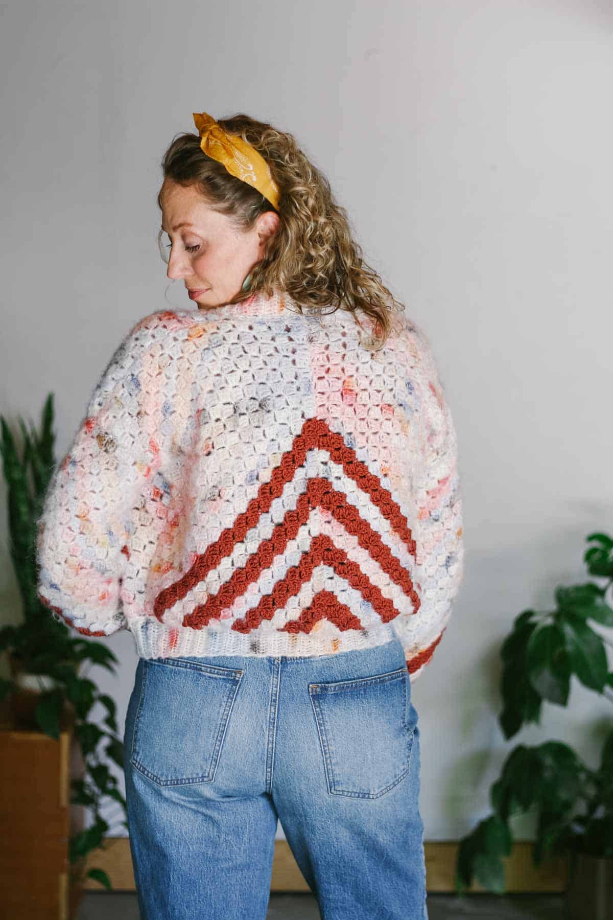 An easy c2c cardigan with an arrow motif worn by a blonde woman with her back to the camera.