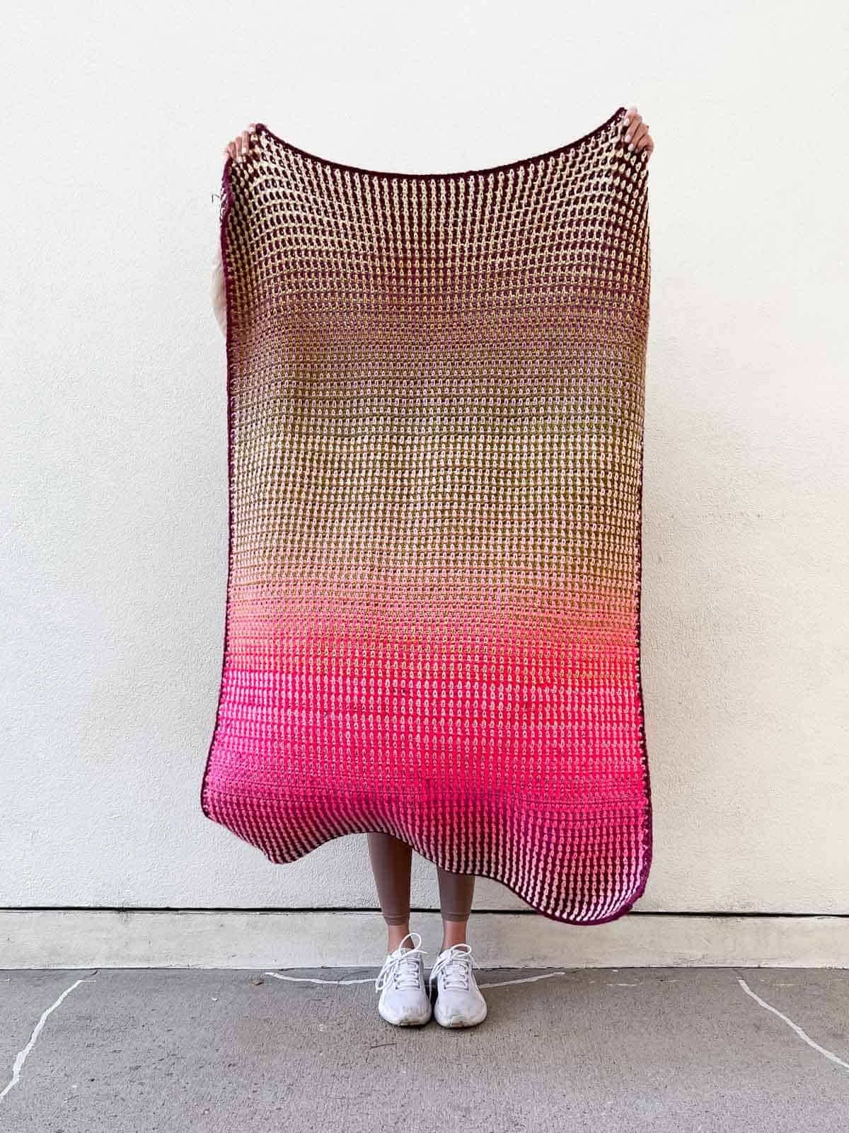 A crochet gradient blanket held by a woman.