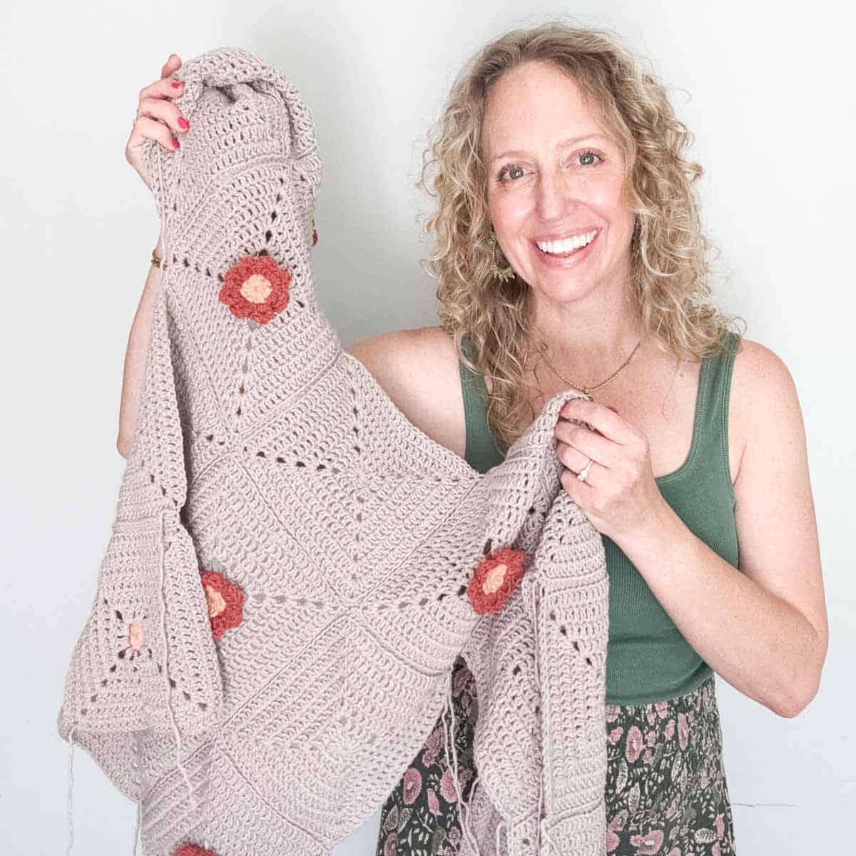 An in-progress crochet cardigan with flower motifs held by a blonde woman.