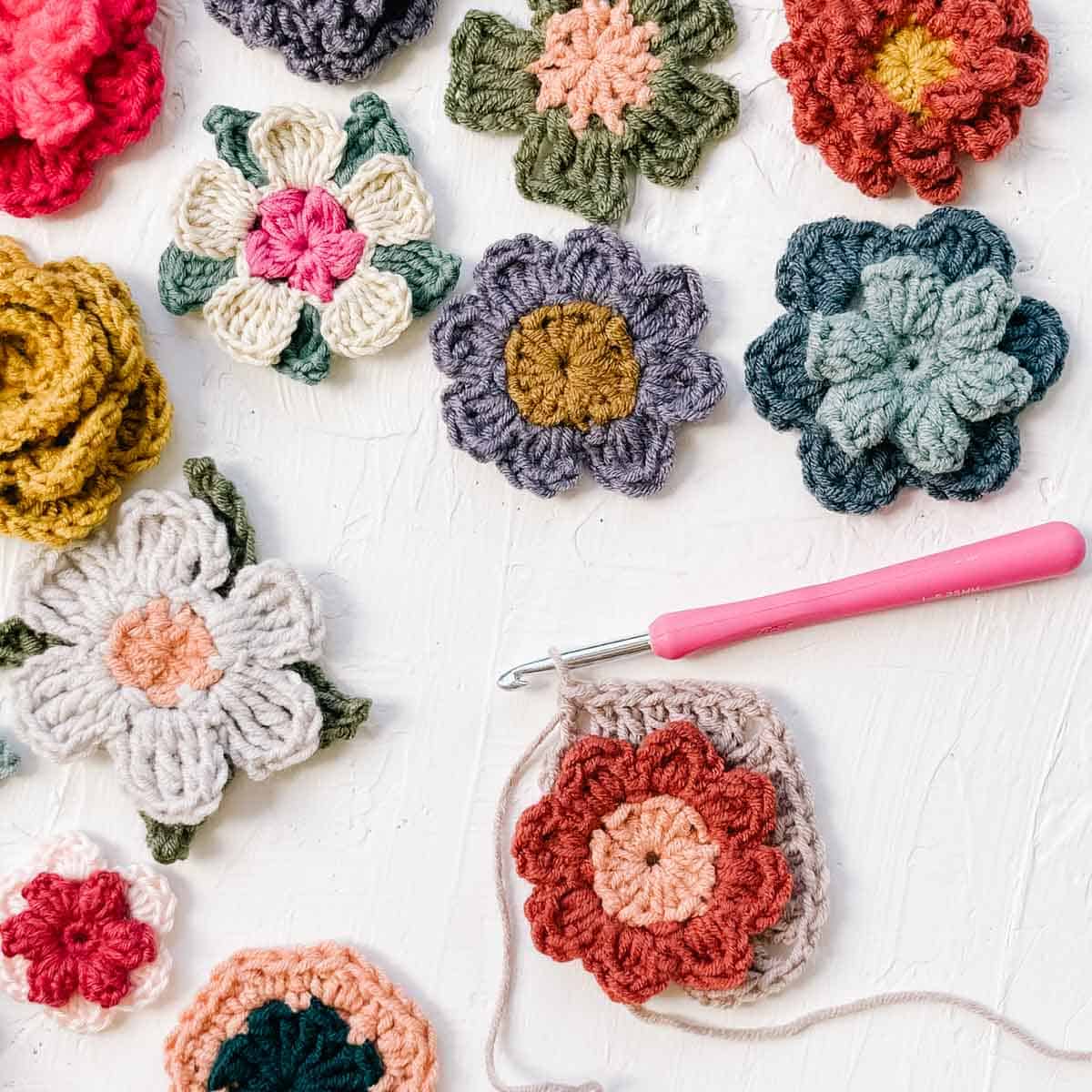 Different flower motifs laid on a table with one in-progress flower with a crochet hook.