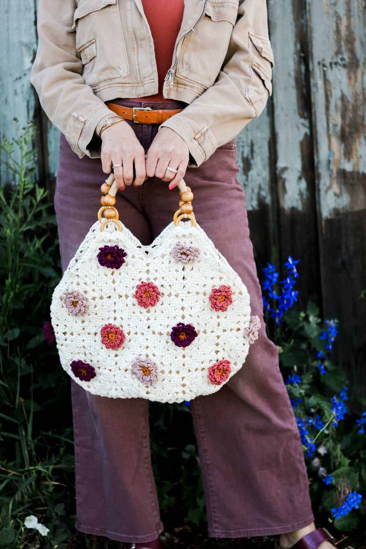 A crochet tote bag with flower motifs and wooden handles held by a woman.