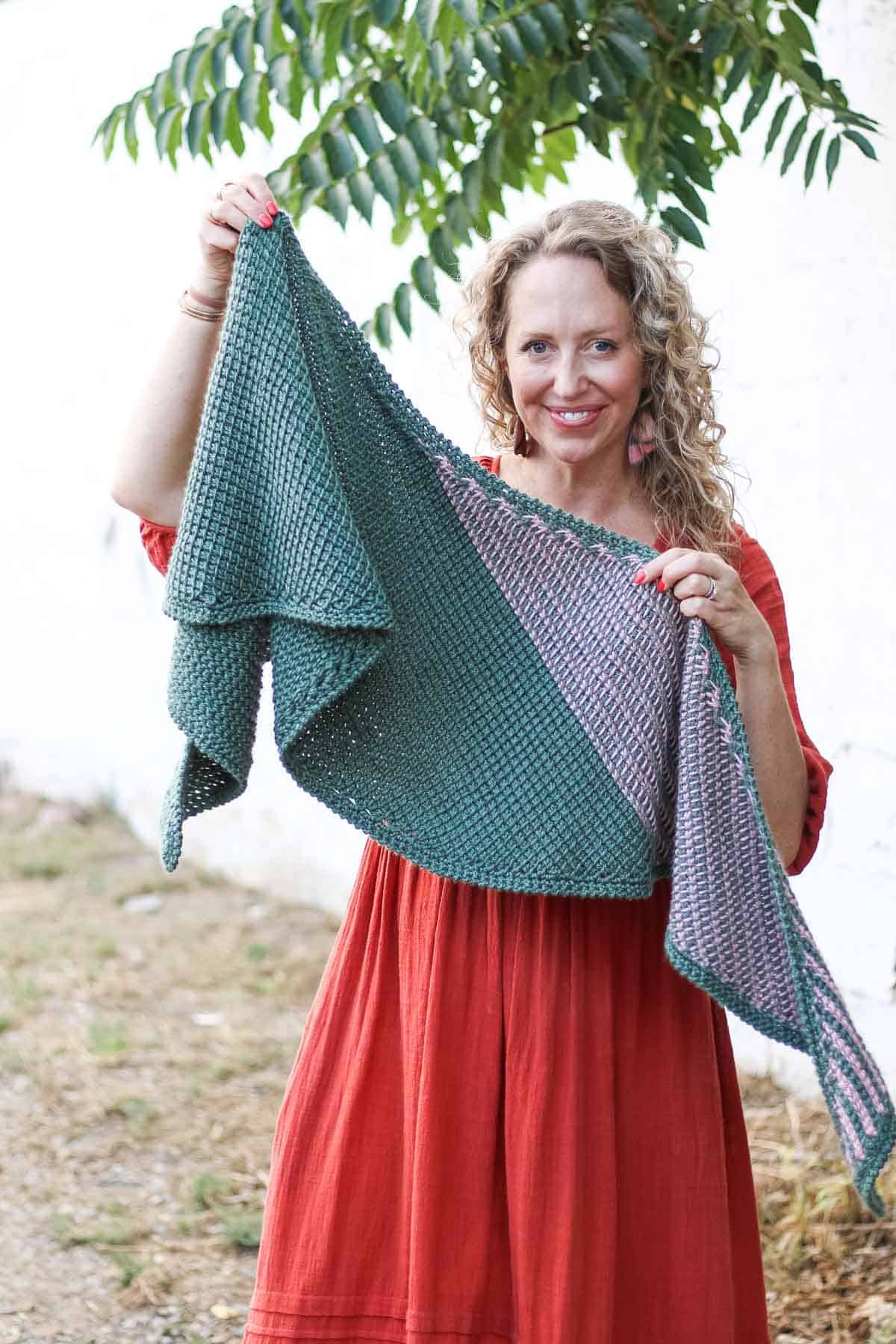 Smiling woman holding a striped Tunisian crochet boomerang shawl.