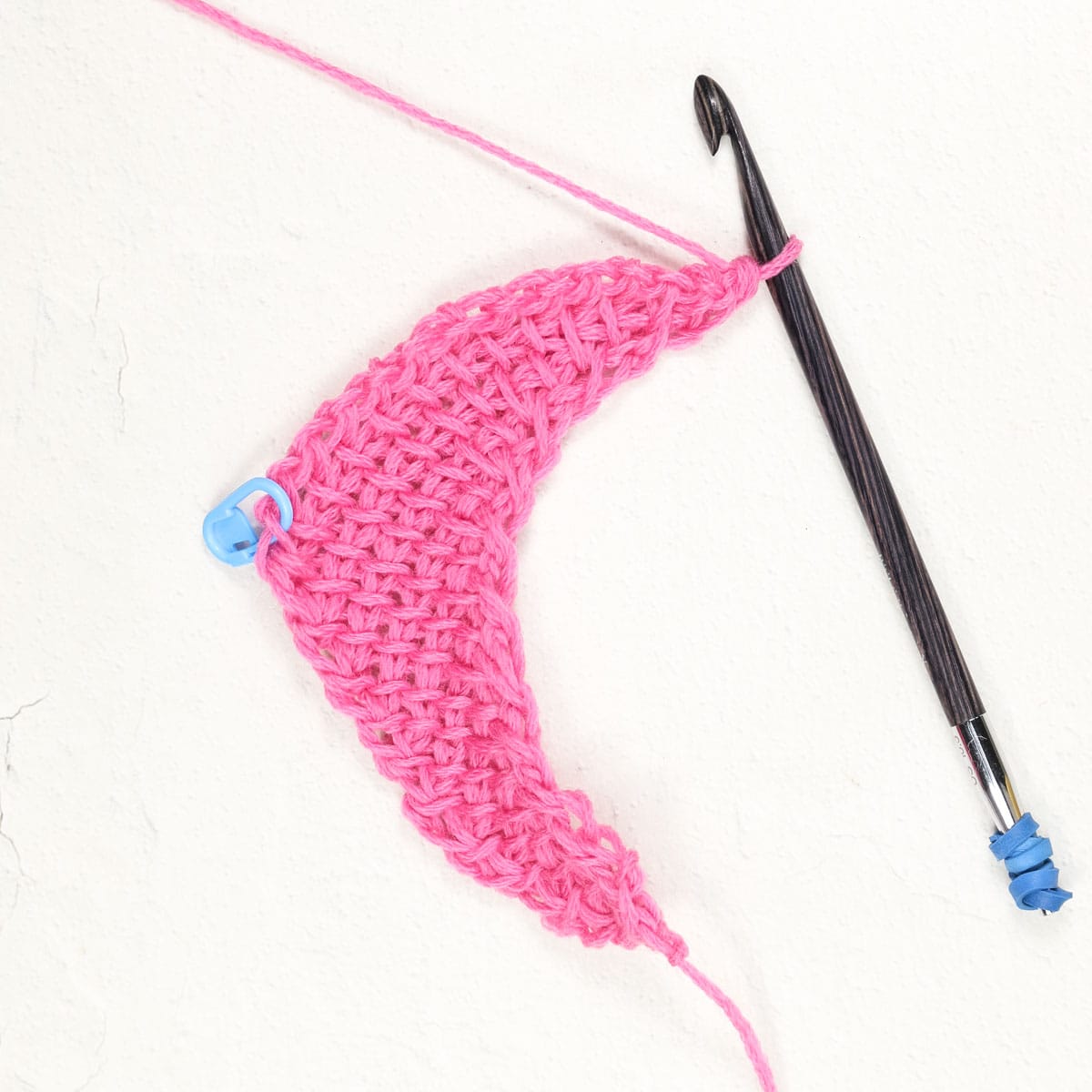 A stitch marker in the last stitch of a row of a Tunisian crochet scarf.