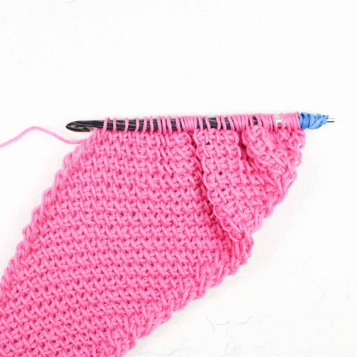 Standard crochet hook with a rubberband on one end being used to Tunisian crochet.