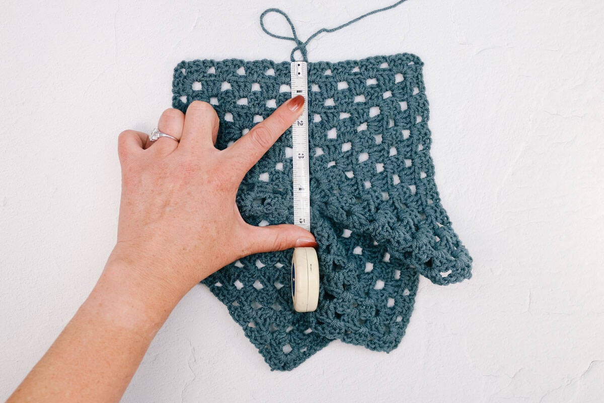 A crochet granny stitch hexagon being measured by a stiff measuring tape.