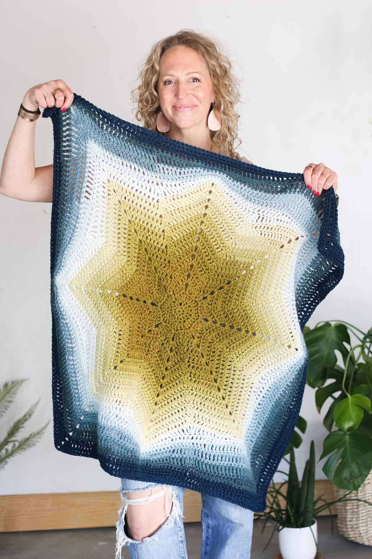 Jess Coppom holding a square crochet blanket with a ripple star in the center.