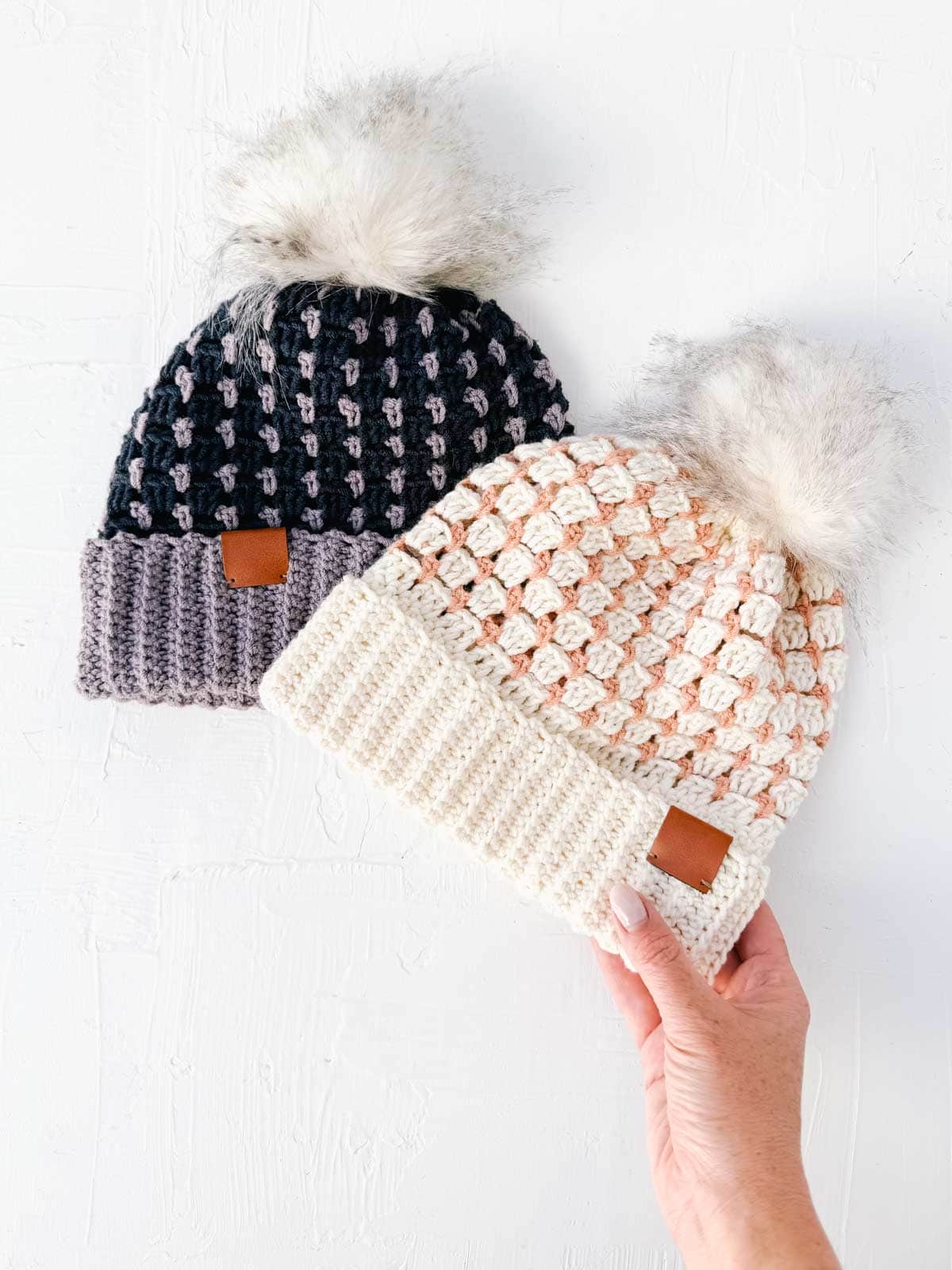 Two multi-color crochet beanies with fur pom poms.