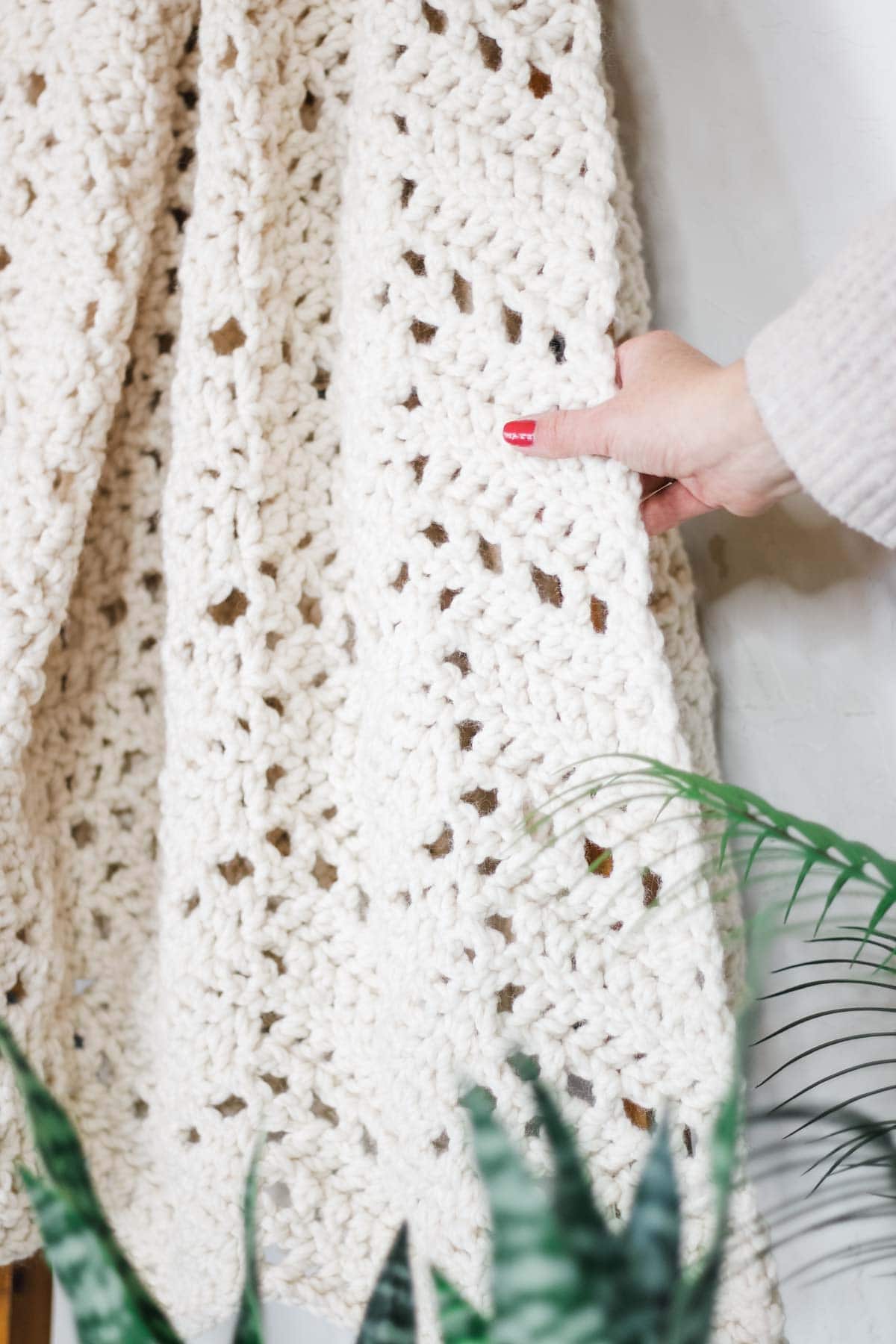 A ripple stitch crochet blanket close-up and a woman's hand holding it.