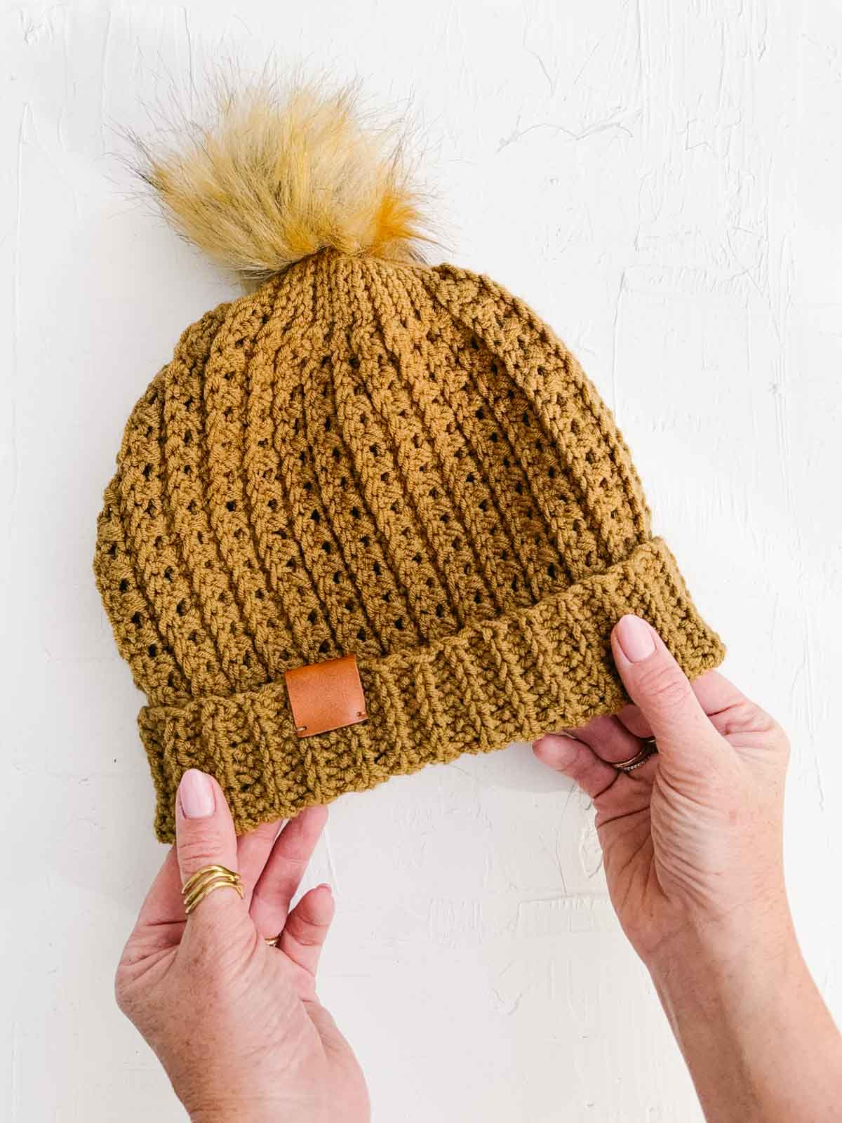 A richly-textured crocheted beanie with a fur pom pom and leather tag.