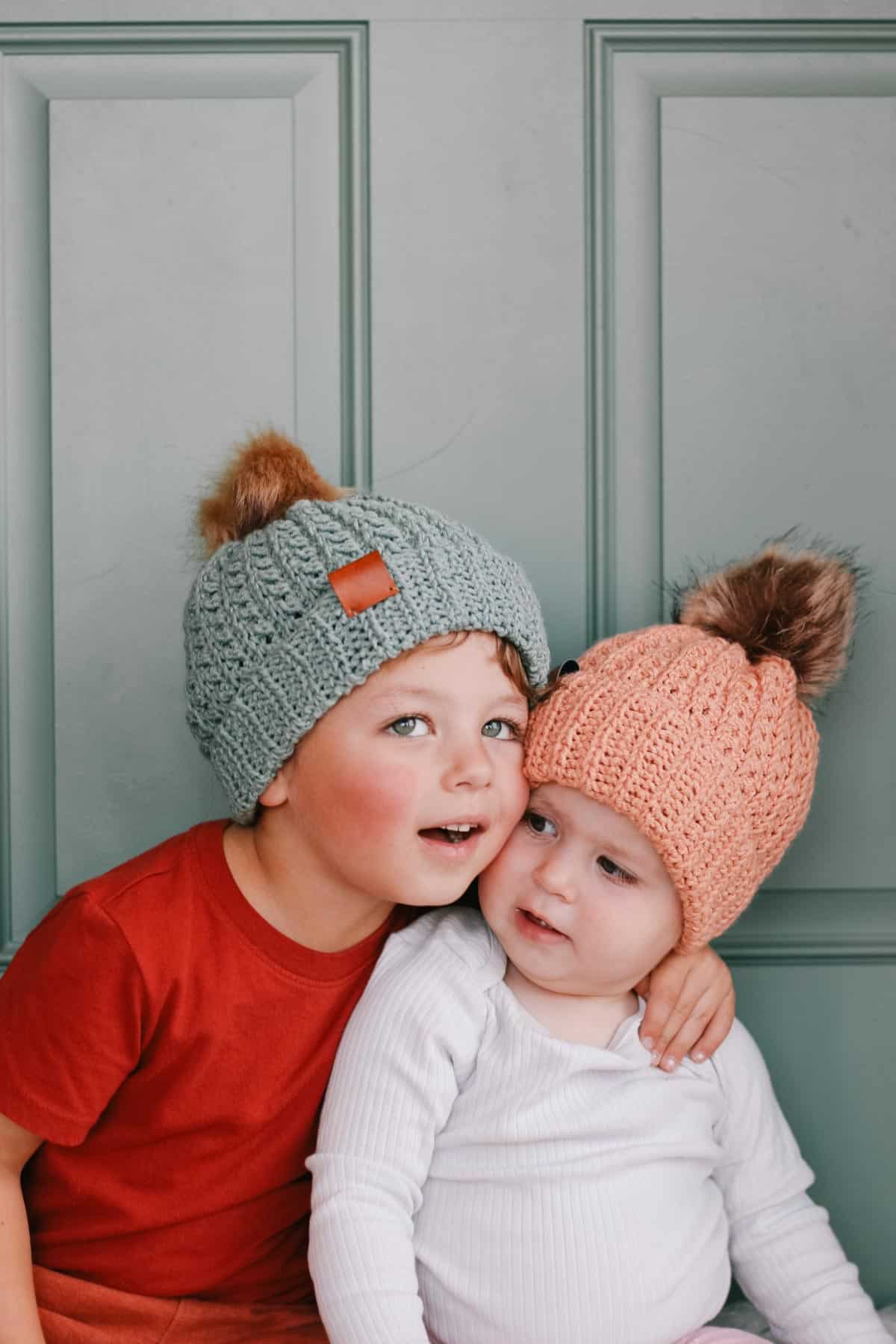 Textured crochet hats with fur pom poms on a toddler and her big brother.