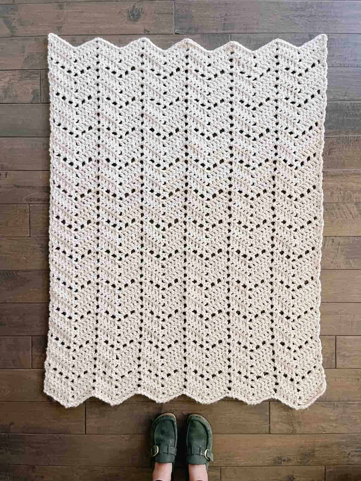 A chunky crochet ripple blanket hanging on a wooden blanket ladder surrounded by plants.