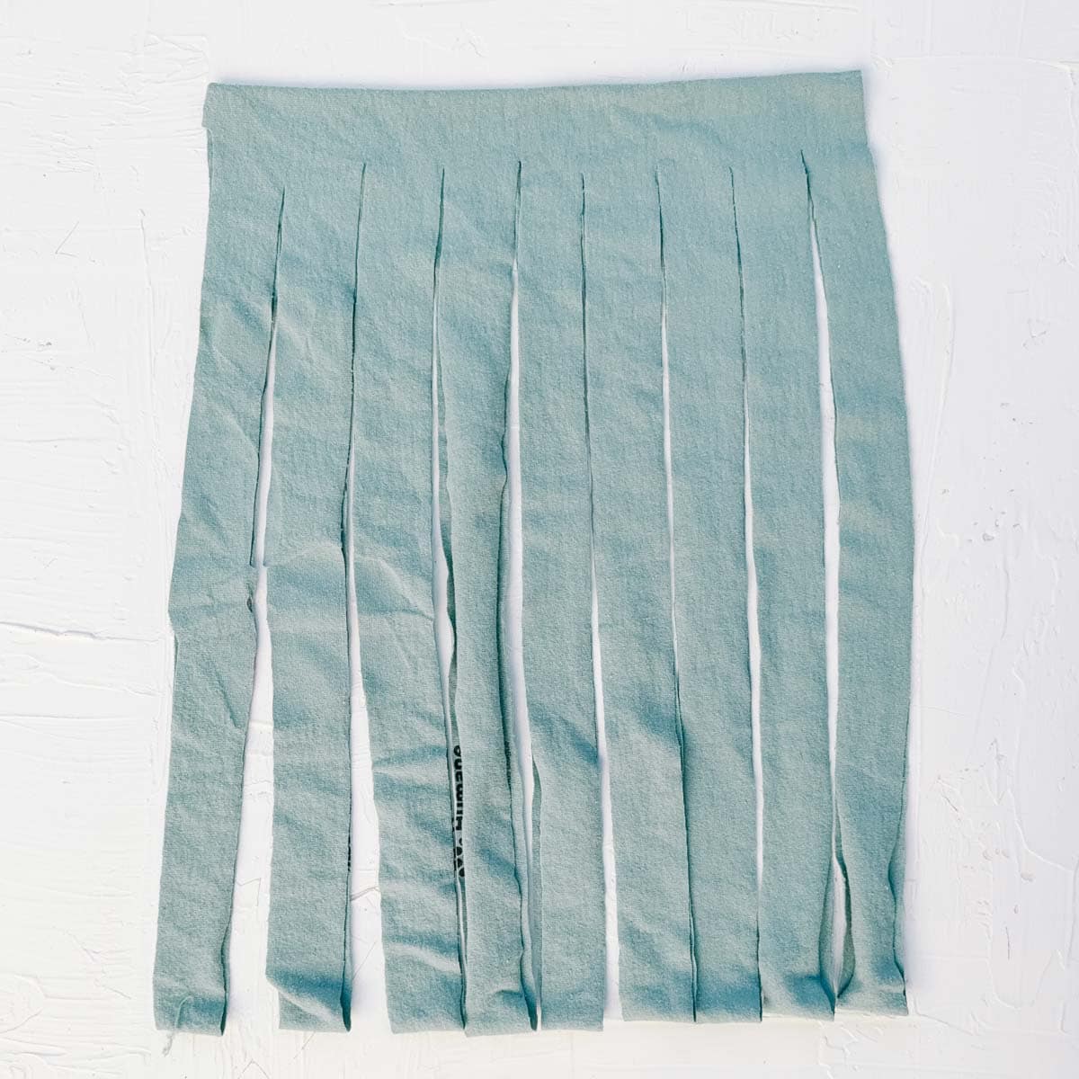 A blue t-shirt cut into fringed strips in the process of creating t-shirt yarn.