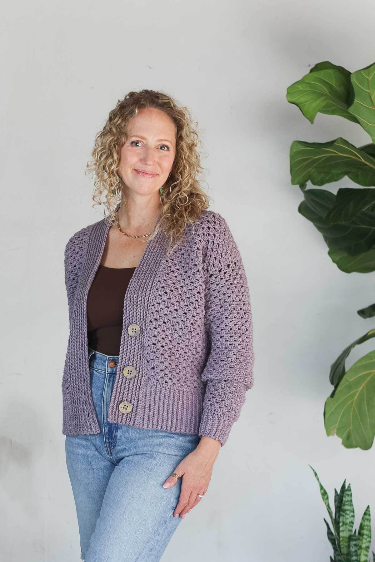 Jess Coppom wearing a dusty lavender crochet cardigan made with Lion Brand Color Theory yarn, buttoned at the front.