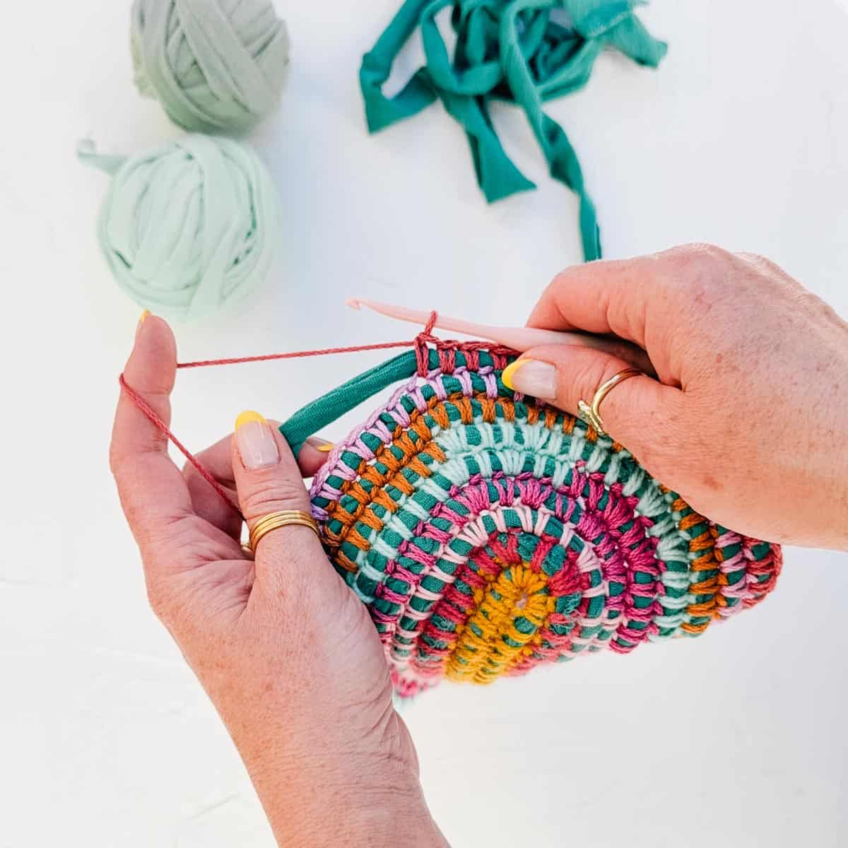 Hands crocheting over a t-shirt yarn core with various colors of scrap yarn.